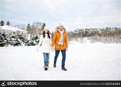 people, season, love and leisure concept - happy couple holding hands and walking along snowy winter field