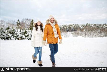 people, season, love and leisure concept - happy couple holding hands and walking along snowy winter field
