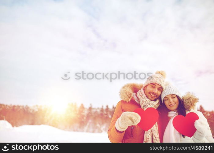 people, season, love and valentines day concept - happy couple holding blank red hearts over winter landscape