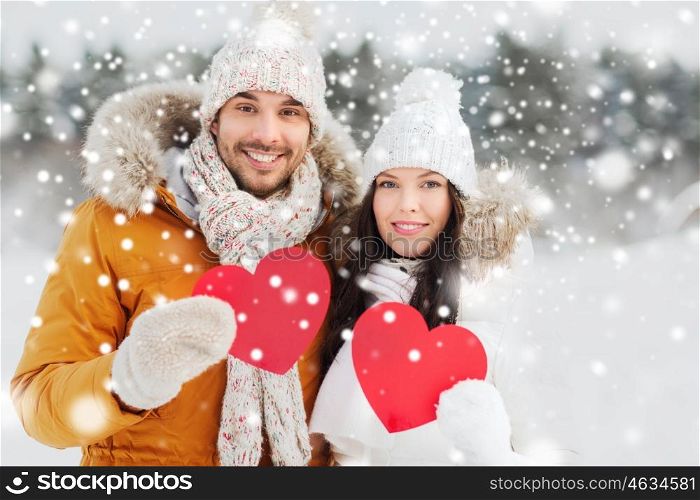 people, season, love and valentines day concept - happy couple holding blank red hearts over winter landscape
