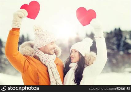 people, season, love and valentines day concept - happy couple holding blank red hearts over winter landscape. happy couple with red hearts over winter landscape