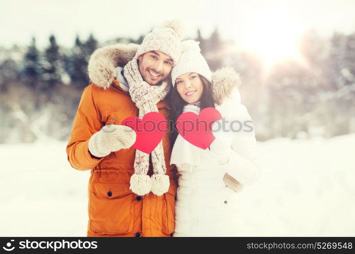 people, season, love and valentines day concept - happy couple holding blank red hearts over winter landscape. happy couple with red hearts over winter landscape