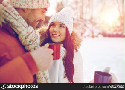 people, season, love, drinks and leisure concept - happy couple holding hot tea cups over winter landscape