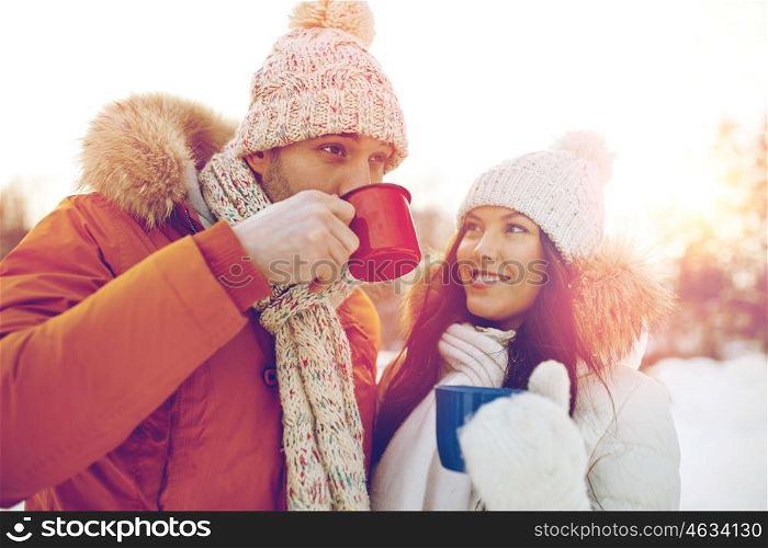 people, season, love, drinks and leisure concept - happy couple holding hot tea cups over winter landscape