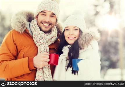 people, season, love, drinks and leisure concept - happy couple holding hot tea cups over winter landscape. happy couple with tea cups over winter landscape