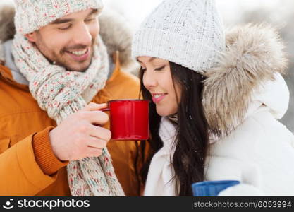 people, season, love, drinks and leisure concept - happy couple holding hot tea cups over winter landscape