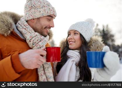 people, season, love, drinks and leisure concept - happy couple holding hot tea cups over winter landscape
