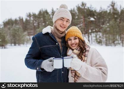 people, season, love, drinks and leisure concept - happy couple with tea cups in snowy winter park. happy couple with tea cups in snowy winter park
