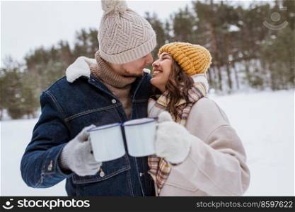 people, season, love, drinks and leisure concept - happy couple with tea cups in snowy winter park. happy couple with tea cups in snowy winter park