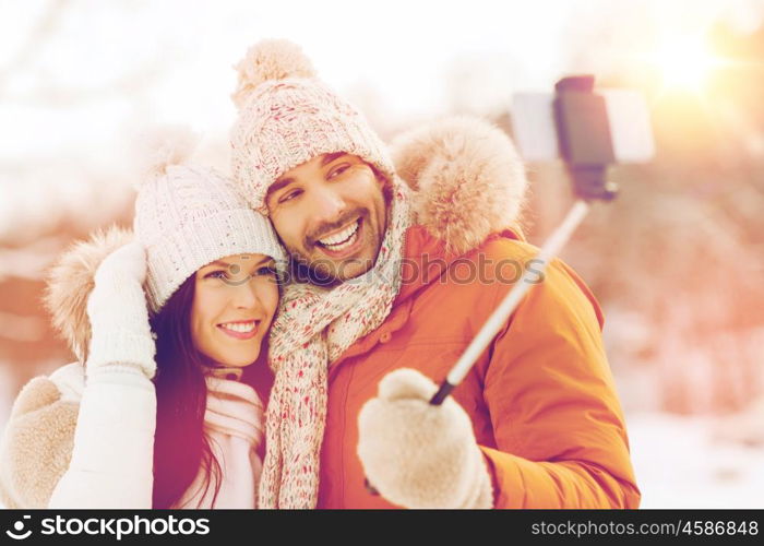 people, season, love, technology and leisure concept - happy couple taking picture with smartphone selfie stick on over winter background