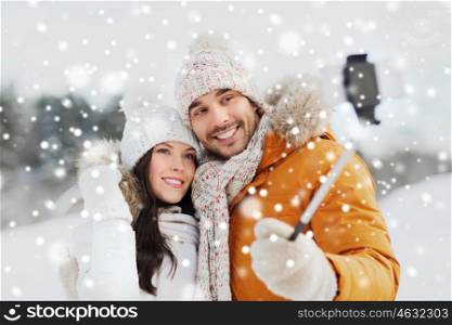people, season, love, technology and leisure concept - happy couple taking picture with smartphone on selfie stick over winter background