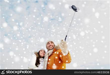 people, season, love, technology and leisure concept - happy couple taking picture with smartphone selfie stick on over winter background