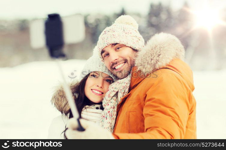 people, season, love, technology and leisure concept - happy couple taking picture with smartphone selfie stick on over winter background. happy couple taking selfie by smartphone in winter