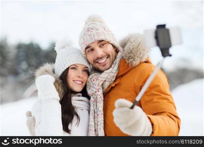 people, season, love, technology and leisure concept - happy couple taking picture with smartphone on selfie stick over winter background