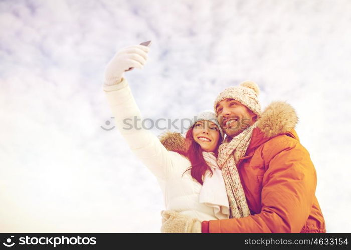 people, season, love, technology and leisure concept - happy couple taking selfie by smartphone over winter background