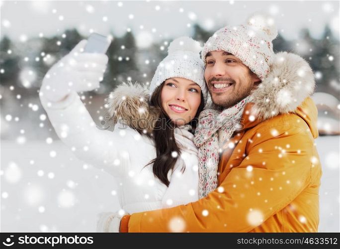 people, season, love, technology and leisure concept - happy couple taking selfie by smartphone over winter background