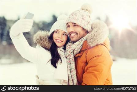 people, season, love, technology and leisure concept - happy couple taking selfie by smartphone over winter background. happy couple taking selfie by smartphone in winter