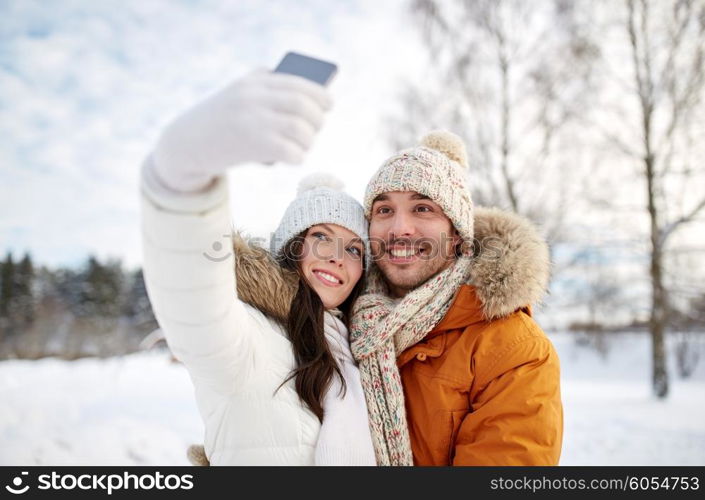 people, season, love, technology and leisure concept - happy couple taking selfie by smartphone over winter background