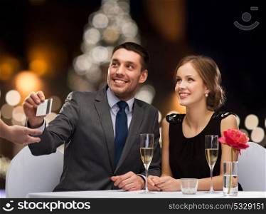 people, service and holidays concept - smiling couple paying for dinner with credit card at restaurant over christmas tree background. couple with credit card at christmas restaurant