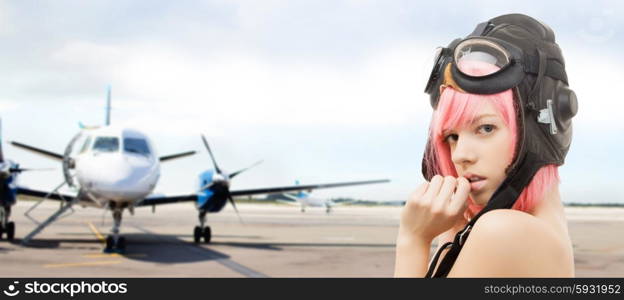 people, sexuality, aviation and role-playing games concept - pink hair girl in aviator helmet over plane in airport background