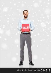 people, shopping, christmas, winter and holidays concept - smiling man holding red sale sign over snow background