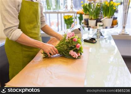 people, shopping, sale, floristry and consumerism concept - close up of florist man wrapping flowers in paper at flower shop