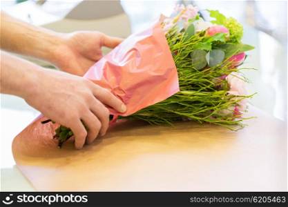 people, shopping, sale, floristry and consumerism concept - close up of florist man wrapping flowers in paper at flower shop