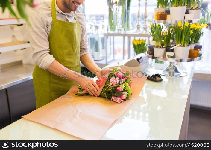 people, shopping, sale, floristry and consumerism concept - close up of happy florist man wrapping flowers in paper at flower shop