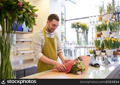 people, shopping, sale, floristry and consumerism concept - happy smiling florist man wrapping flowers in paper at flower shop