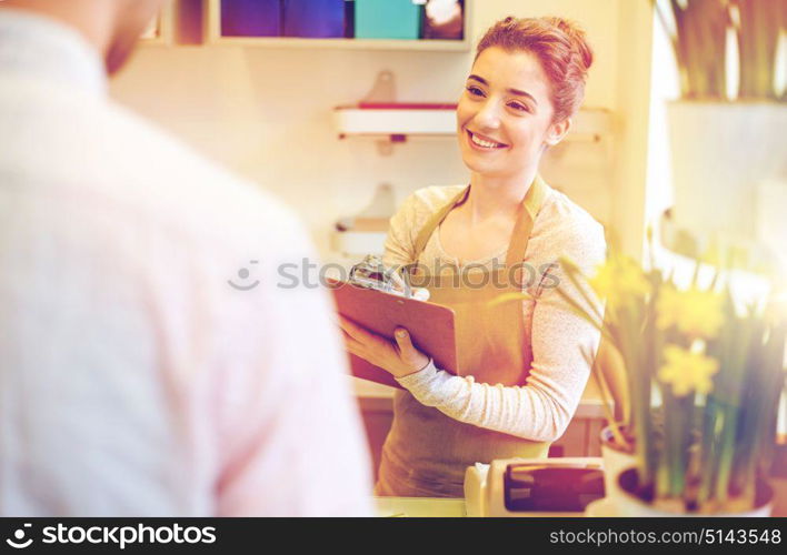 people, shopping, sale, floristry and consumerism concept - happy smiling florist woman with clipboard and man or customer making order at flower shop. florist woman and man making order at flower shop