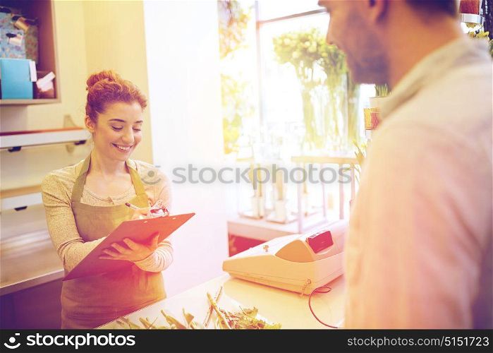 people, shopping, sale, floristry and consumerism concept - happy smiling florist woman with clipboard and man or customer making order at flower shop. florist woman and man making order at flower shop