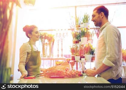 people, shopping, sale, floristry and consumerism concept - happy smiling florist woman and man or customer talking at flower shop. smiling florist woman and man at flower shop