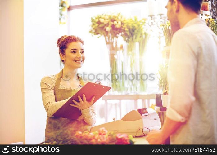 people, shopping, sale, floristry and consumerism concept - happy smiling florist woman with clipboard and man or customer making order at flower shop. florist woman and man making order at flower shop