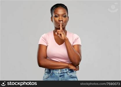 people, silence and secret concept - african american young woman with finger on lips over grey background. african american woman with finger on lips