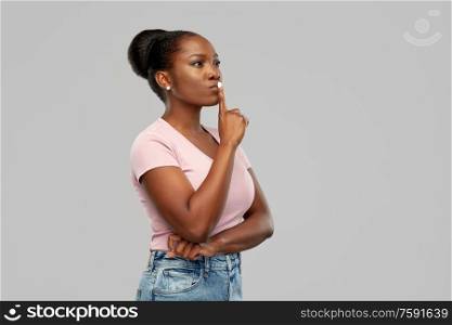 people, silence and secret concept - african american young woman with finger on lips over grey background. african american woman with finger on lips