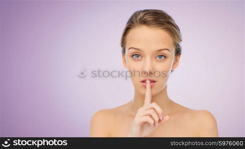 people, silence, secret, gesture and beauty concept - beautiful young woman holding finger on lips over violet background