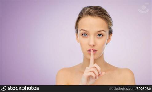 people, silence, secret, gesture and beauty concept - beautiful young woman holding finger on lips over violet background