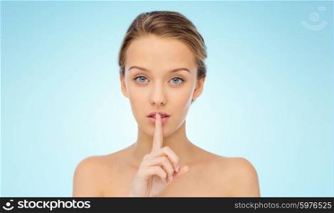 people, silence, secret, gesture and beauty concept - beautiful young woman holding finger on lips over blue background