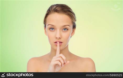 people, silence, secret, gesture and beauty concept - beautiful young woman holding finger on lips over green natural background