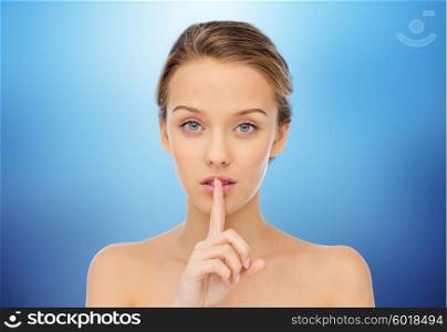 people, silence, secret, gesture and beauty concept - beautiful young woman holding finger on lips over blue background