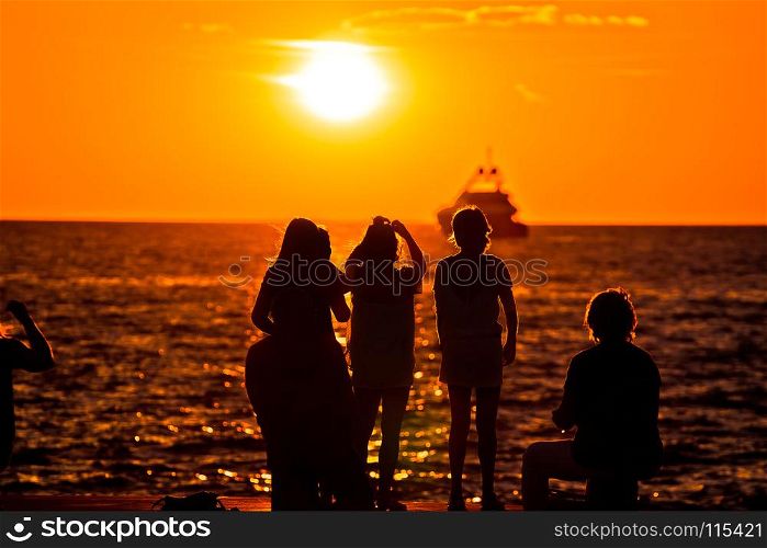 People silhouettes at golden sunset at sea and yacht on horizon, Zadar, Croatia