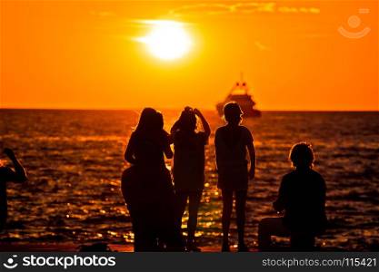 People silhouettes at golden sunset at sea and yacht on horizon, Zadar, Croatia