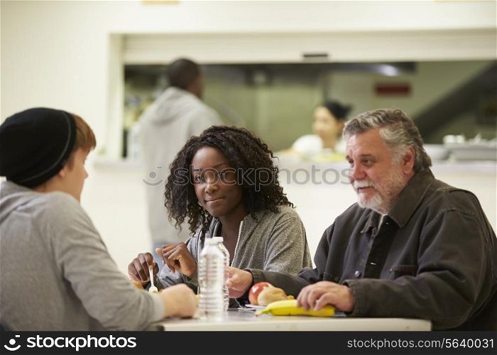 People Sitting At Table Eating Food In Homeless Shelter