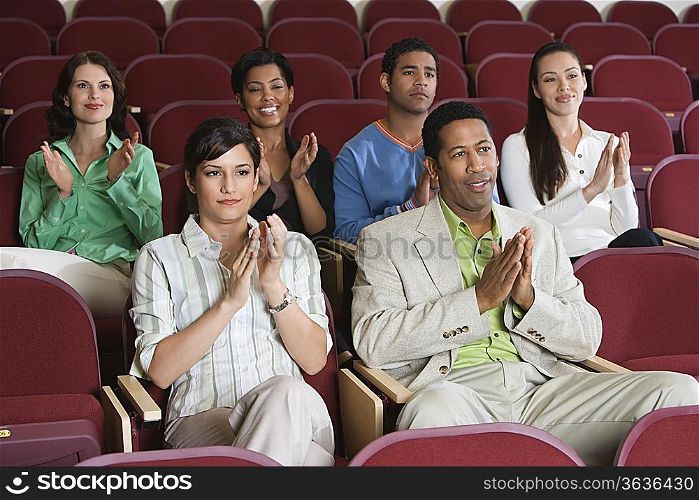 People sitting in auditorium and clapping hands