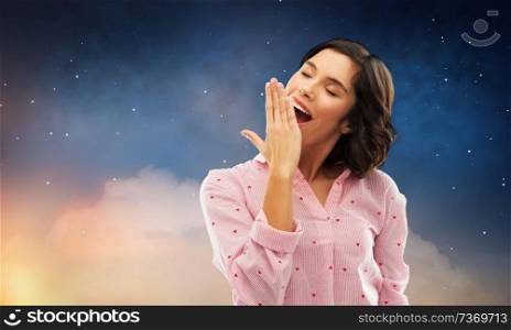 people, sleeping and bedtime concept - happy young sleepy woman in pajama yawning over starry night sky background. sleepy woman in pajama yawning over night sky
