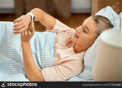people, sleeping and rest concept - smiling girl with smart watch lying in bed at home. smiling girl with smart watch lying in bed at home