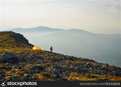 People spending summer vacation in mountains, standing by tent looking at sunrise over valley. Active couple hiking in mountains. Yellow tent put over valley. Foggy mountain landscape view at sunrise