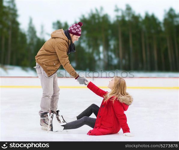 people, sport and leisure concept - smiling man helping women to rise up on skating rink over winter outdoor background. man helping woman to rise up on skating rink