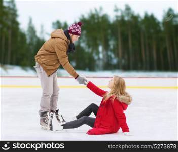 people, sport and leisure concept - smiling man helping women to rise up on skating rink over winter outdoor background. man helping woman to rise up on skating rink