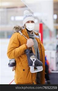 people, sport and leisure concept - young man wearing face protective medical mask for protection from virus disease with ice-skates on skating rink. young man in mask with ice-skates on skating rink